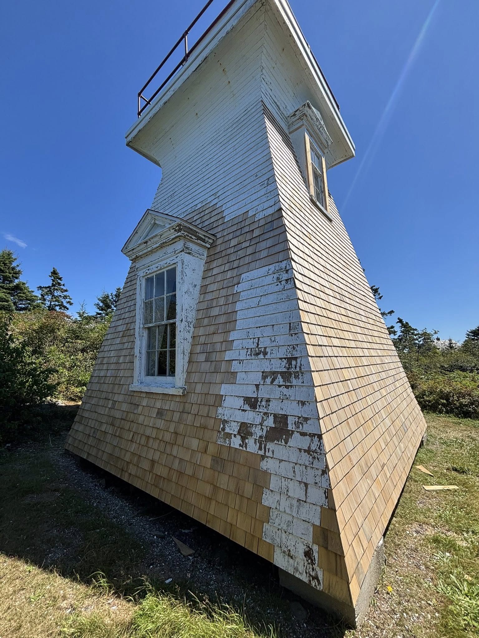 Shingled lighthouse with peeling paint and bare shingles before restoration
