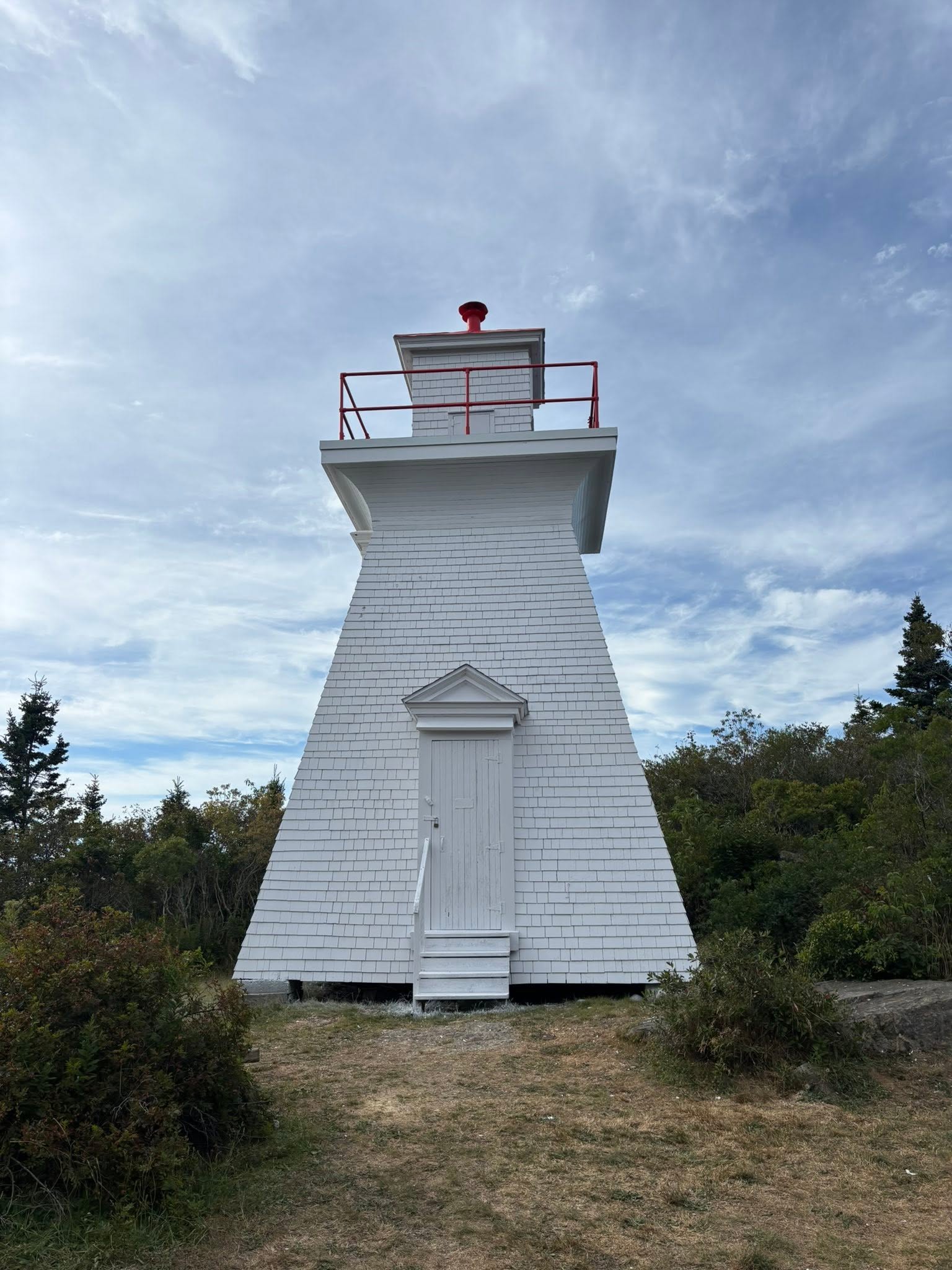 Restored white shingled heritage lighthouse with fresh red trim