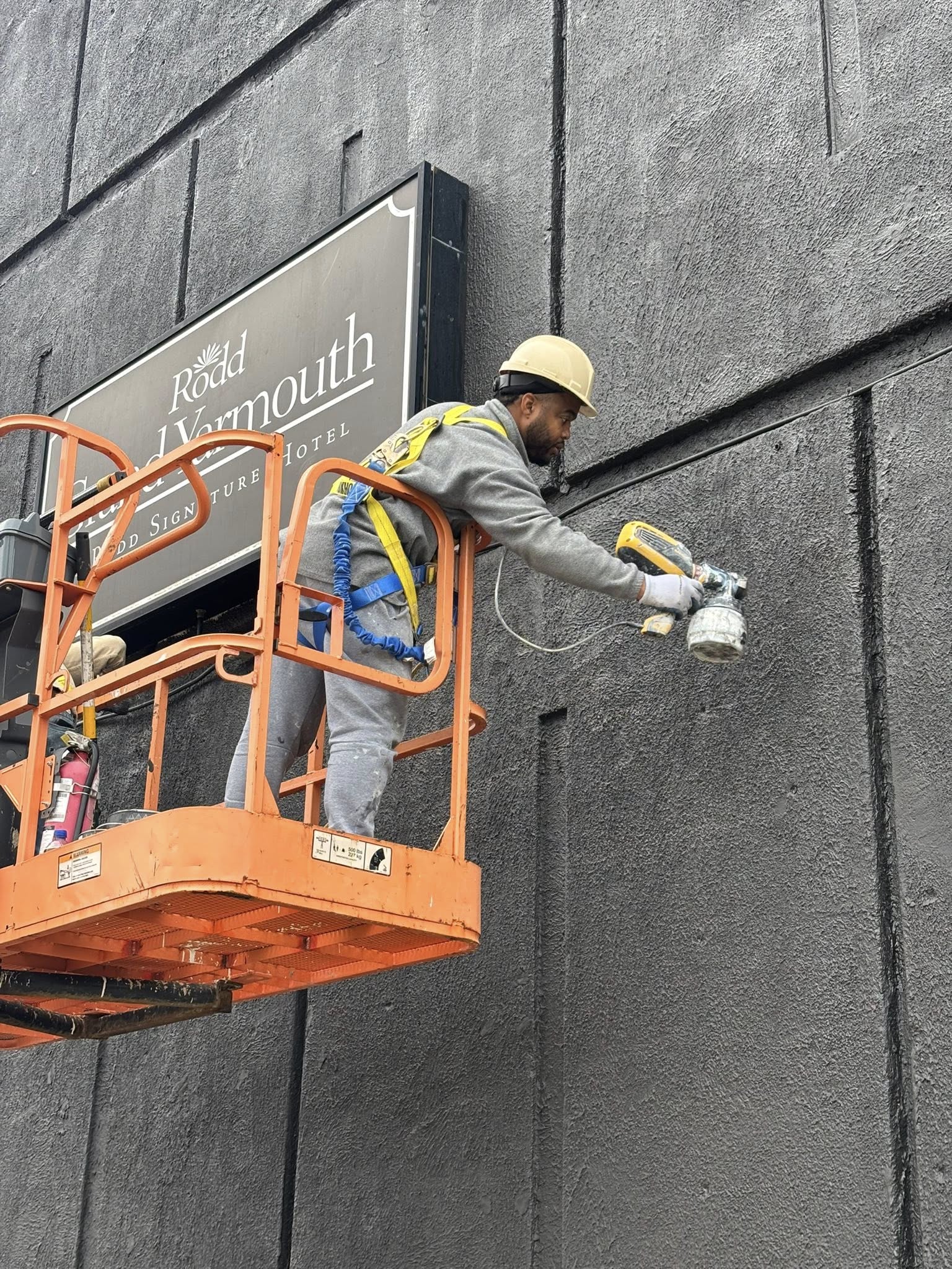 Dutch Painting Services technician spray-painting a commercial building exterior from a lift